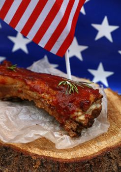 Portion of cooked pork spare ribs in bbq sauce on paper parchment and wood cut under American flag, close up, high angle view