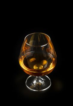 Close up one glass of cognac or brandy isolated on black background, high angle view