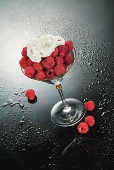 Glass with raspberries and cream on a glass background