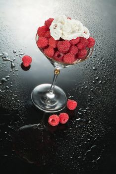 Glass with raspberries and cream on a glass background