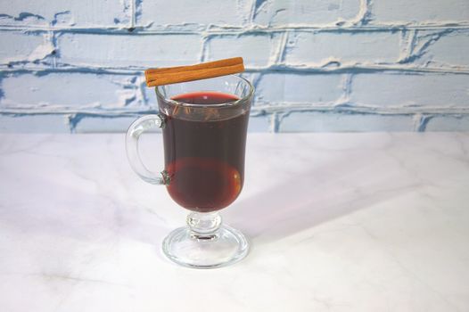 A glass of hot mulled wine with a cinnamon stick on top. Close-up.