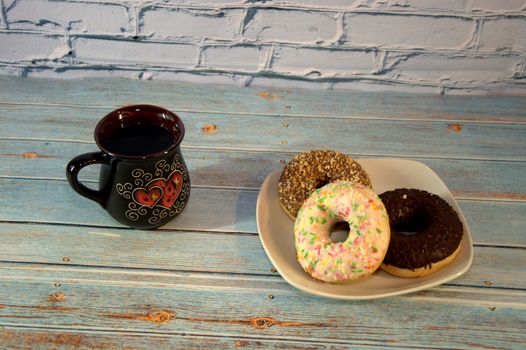 Plate with several multi-colored donuts in the glaze and a dark ceramic cup with tea. Close-up.