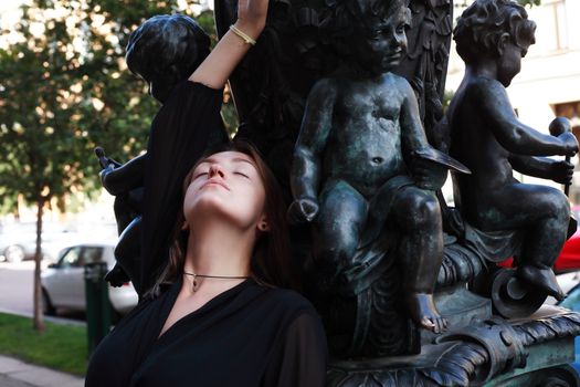 Beautiful young woman near old iron sculpture with angels