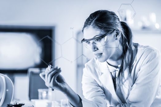 Portrait of a confident female health care expert in life science laboratory writing structural chemical formula on a glass board. Healthcare and modern life science concept. Blue toned image.