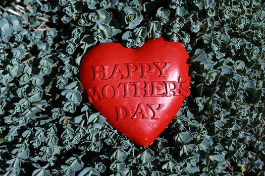 The picture shows a happy mother`s day heart in the garden.