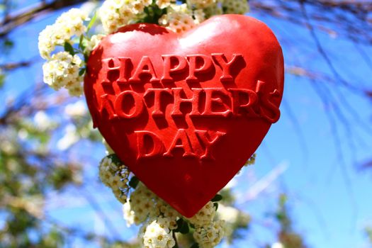 The picture shows a red heart with the text happy mother`s day in the snowberry bush.