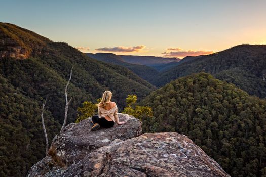 Woman high on a rocky outcrop with views of the sunset over mountain valley gorge.