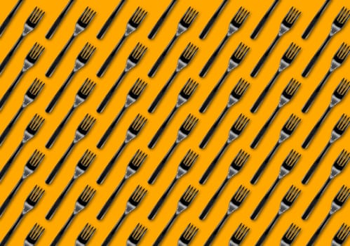 Many black plastic forks on yellow background, top view. Disposable table wear concept. Creative top view pattern.