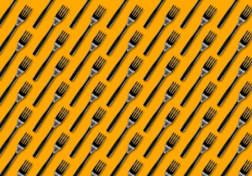 Many black plastic forks on yellow background, top view. Disposable table wear concept. Creative top view pattern.