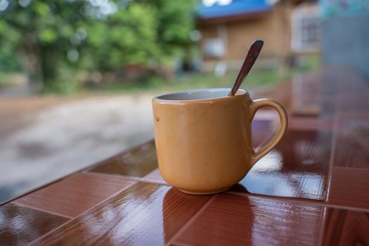 A Cup of latte coffee in white cup on tile desk with blurred chairs in the background