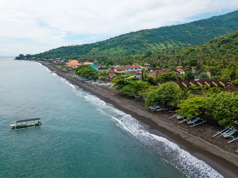 Aerial view of Amed beach in Bali, Indonesia. Traditional fishing boats called jukung on the black sand beach and one on the sea.