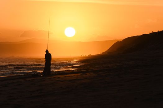 Sun setting on an African south coast beach with girl and fishing rod silhouette, Mossel Bay, South Africa