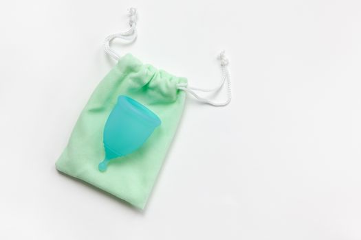 Turquoise menstrual cup on green small bag on white background. Concept zero waste, savings, minimalism, these days. Feminine hygiene product, flat lay, copy space. Horizontal.