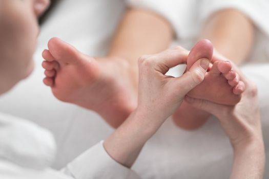 Professional female masseur giving reflexology massage to woman foot.