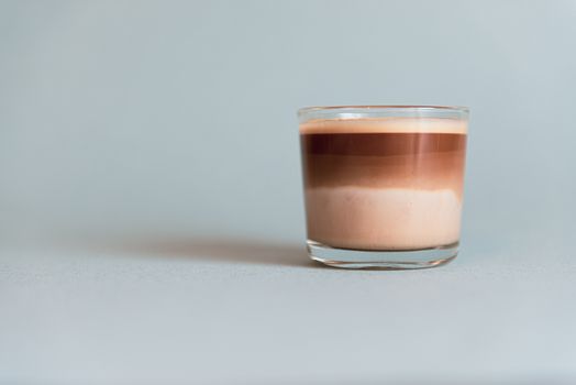 Mini cup of multilayer coffee in a glass cup on grey background.