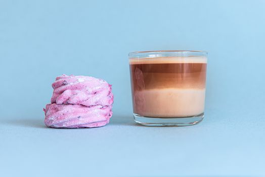 Mini cup of multilayer coffee in a glass cup on blue background with pink cake.