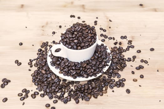 Many coffee beans on wooden background and white cup