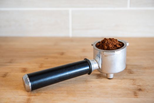 Filter holder with ground coffee on wooden table.