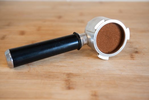 portafilter with temping ground coffee on wooden table.