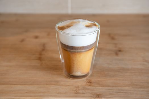 multilayer coffee or cappuccino in a glass cup on wooden table.