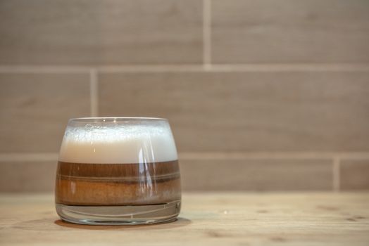 multilayer coffee or cappuccino in a glass cup on wooden table.