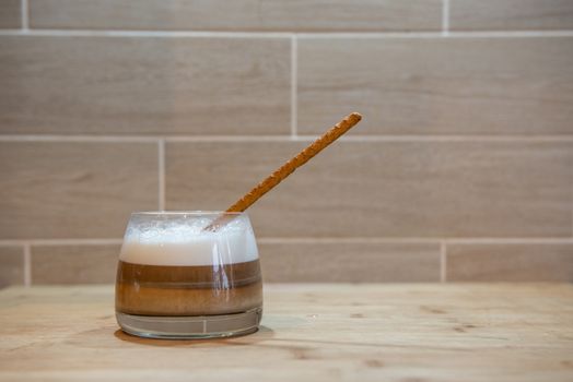 multilayer coffee or cappuccino in a glass cup on wooden table. With bread straw