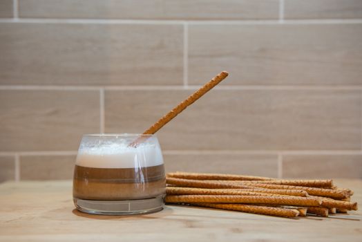 multilayer coffee or cappuccino in a glass cup on wooden table. With bread straw