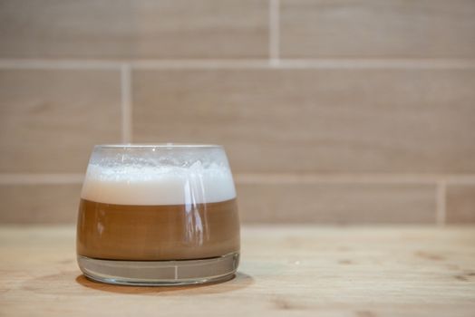 multilayer coffee or cappuccino in a glass cup on wooden table.