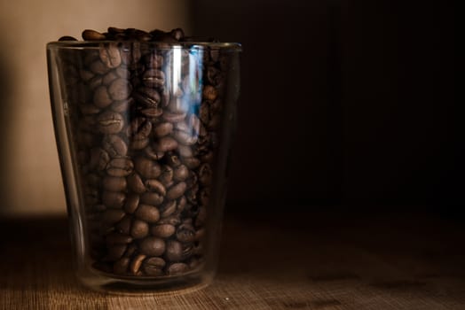 Many coffee beans in glass of cup on wooden and black background