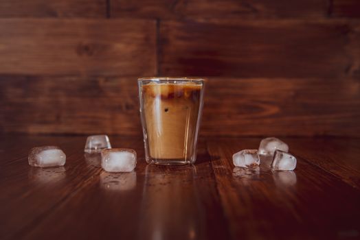 coffee with milk and ice on wooden background. With ice cubes on table.