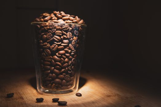 Many coffee beans in glass of cup on wooden and black background