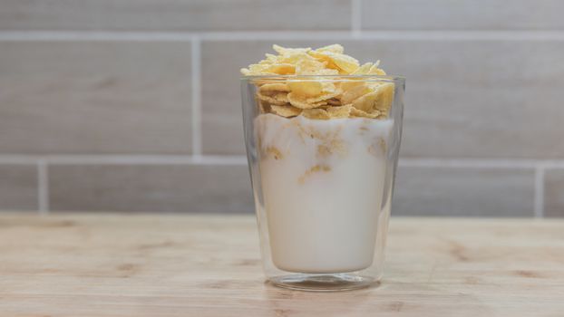 Corn flakes with milk in glass cup.