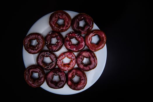 assorted donuts with chocolate frosted, pink glazed and sprinkles donuts. Donuts on white plate with black background