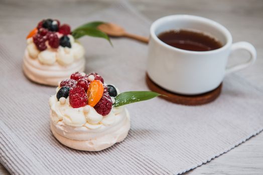 Pavlova meringue desert cake with cream, small fruits and cup of tea