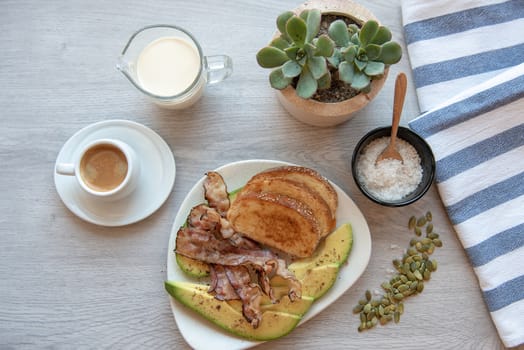 Fried bacon on white plate with cup of coffee, milk jug and toast. Breakfast on gray table