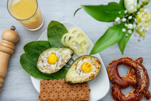 Eggs baked in avocado on plate with onion, juicy and pretzel