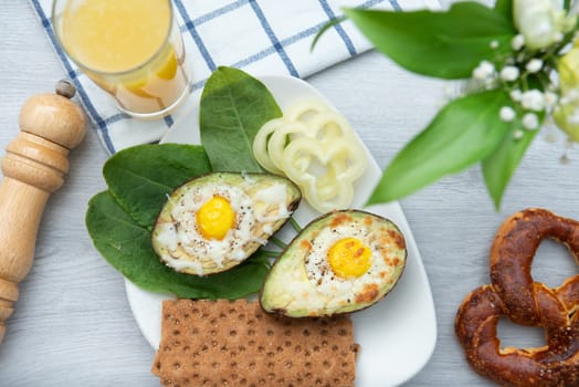 Eggs baked in avocado on plate with onion, juicy and pretzel