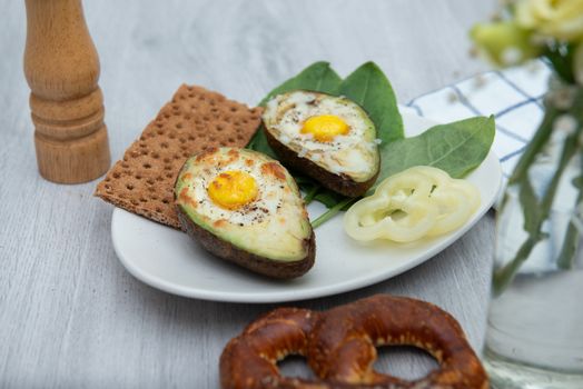 Eggs baked in avocado on plate with pretzel