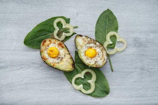 Two Eggs baked in avocado on wooden tabel and green leaves.