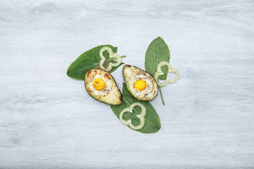 Two Eggs baked in avocado on wooden tabel and green leaves.