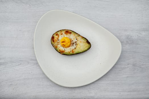 one egg baked in avocado on wooden table and white plate