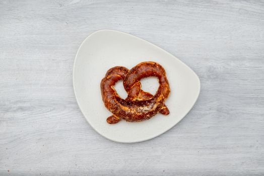 one pretzel on white plate and wooden table