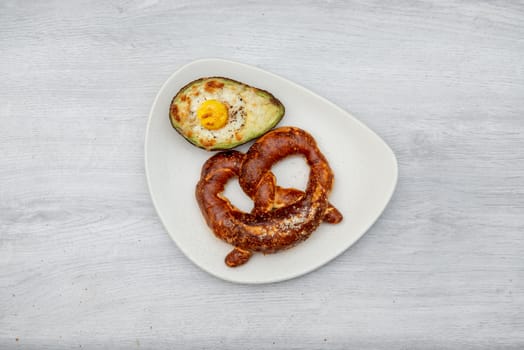 Eggs baked in avocado on plate with pretzel.