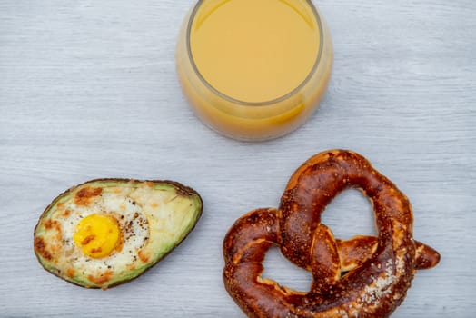 Eggs baked in avocado on wooden table with pretzel and juicy