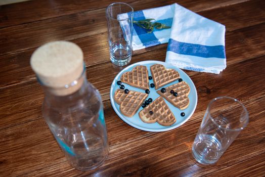 an empty bottle, two glasses and wafers on a plate. Wooden background