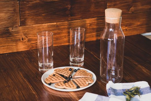 an empty bottle, two glasses and wafers on a plate. Wooden background