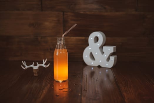 a vintage bottle of freshly squeezed juice on a wooden background and a glowing ampersand. Near wine cork decorated with deer antlers.