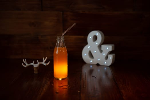 a vintage bottle of freshly squeezed juice on a wooden background and a glowing ampersand. Near wine cork decorated with deer antlers.