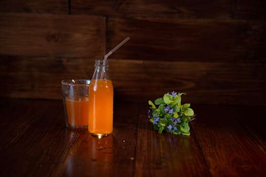 vintage bottle with juice, straw and flowers on wooden table.