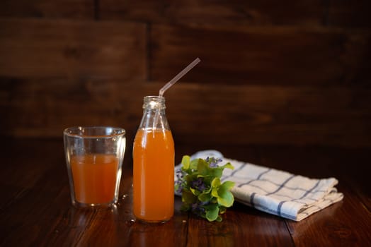 vintage bottle with juice, straw, flowers and towel on wooden table.